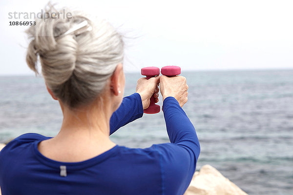 Reife Frau am Meer  mit Handgewichten trainierend  Rückansicht