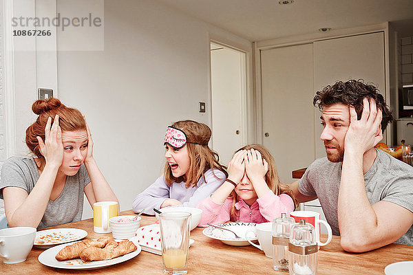 Müde mittlere erwachsene Eltern am Frühstückstisch mit zwei Töchtern