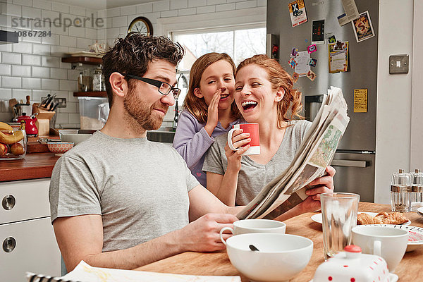 Mittelgroßer Mann am Frühstückstisch  der Zeitung liest  während Tochter und Mutter lachen