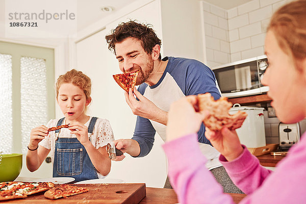 Mittelgroßer erwachsener Mann isst Pizza mit Töchtern an der Küchenbank