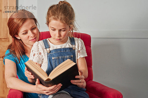 Mittlere erwachsene Frau liest Buch mit Tochter auf Sessel