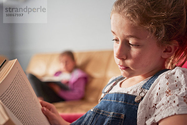 Nahaufnahme eines Mädchens und seiner Schwester beim Lesen von Büchern im Wohnzimmer