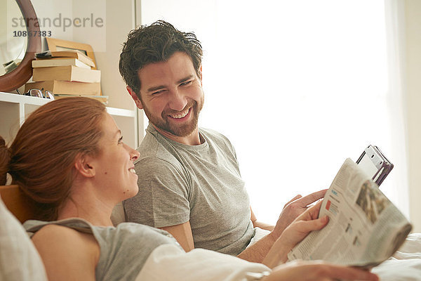 Mittelgroßes erwachsenes Paar liest Einblattdruck und digitales Tablett im Bett