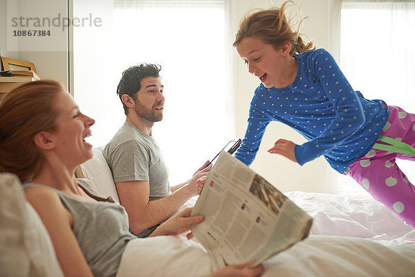 Mittelgroßes erwachsenes Paar liest Einblattdruck  während die Tochter auf das Bett springt