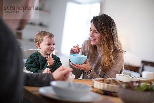 Eltern füttern am Esstisch lächelndes Baby