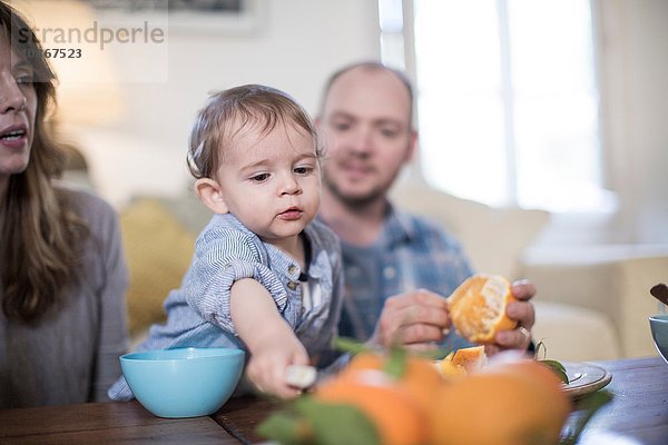 Eltern essen mit dem Baby zu Mittag  schälen Orange