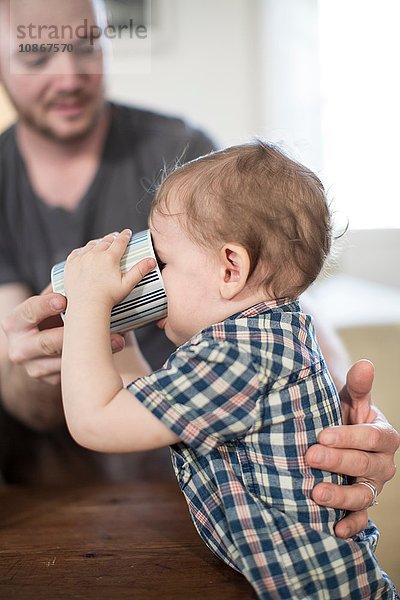 Vater hilft kleinem Jungen  aus Becher zu trinken