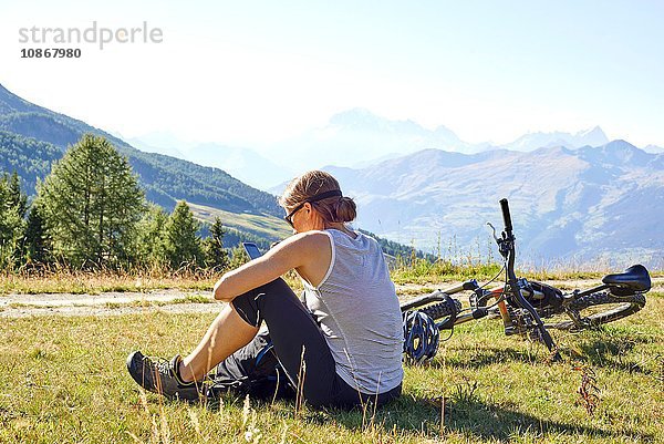 Mountainbikerin sitzt in Berglandschaft und liest Smartphone-Texte  Aostatal  Aosta  Italien