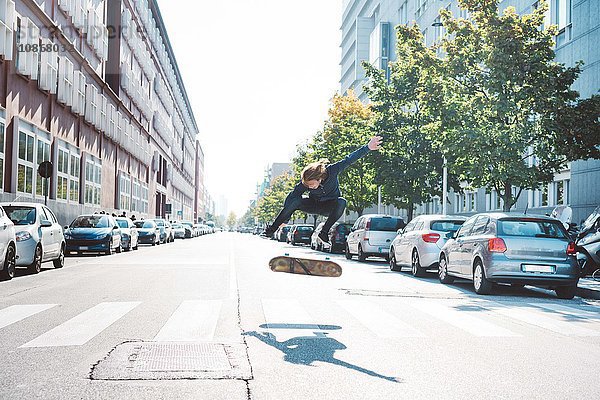 Junge männliche Skateboarder aus der Stadt springen in der Luft auf dem Fußgängerüberweg