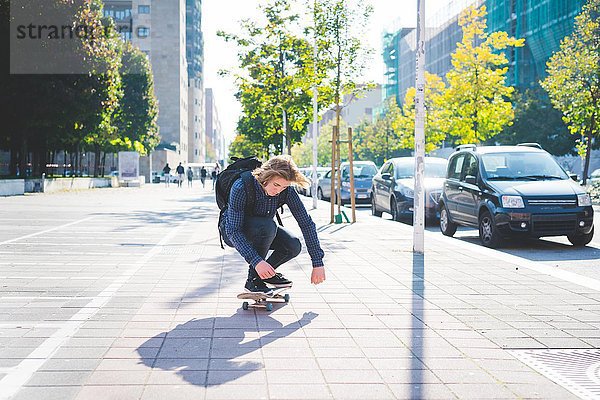 Junge männliche Skateboarder hocken beim Skateboarden auf dem Bürgersteig