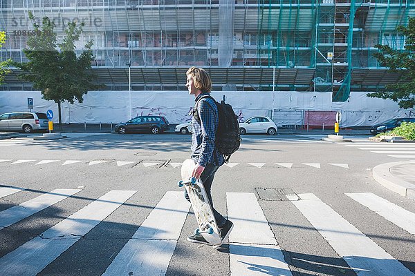 Junger Mann überquert Fußgängerüberweg mit Skateboard