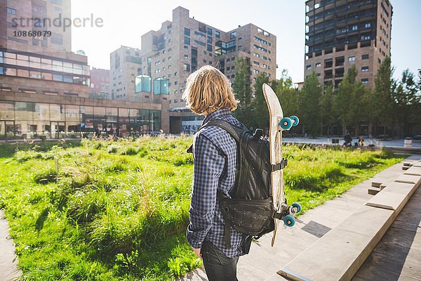 Junge männliche Skateboarder mit Rucksack und Skateboard