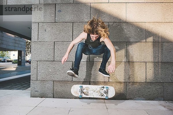 Junger männlicher Skateboarder beim Skateboarden Sprungtrick über Skateboard