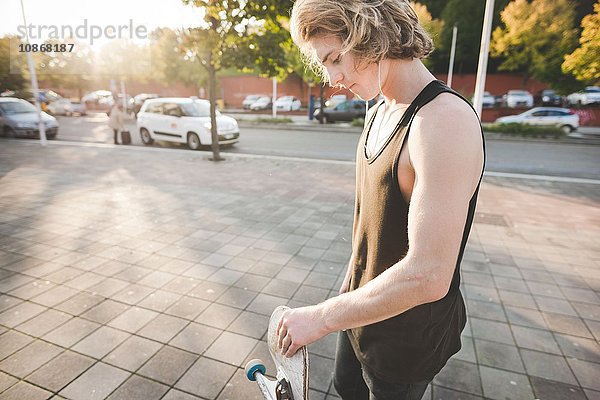 Junge männliche Stadtskateboarder hören Kopfhörermusik auf dem Bürgersteig