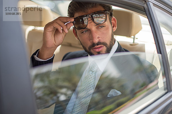Junger Geschäftsmann hält Sonnenbrille auf dem Rücksitz eines Autos hoch  Dubai  Vereinigte Arabische Emirate