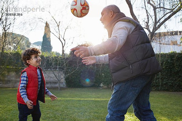 Grossvater und Enkel spielen lächelnd mit Fussball