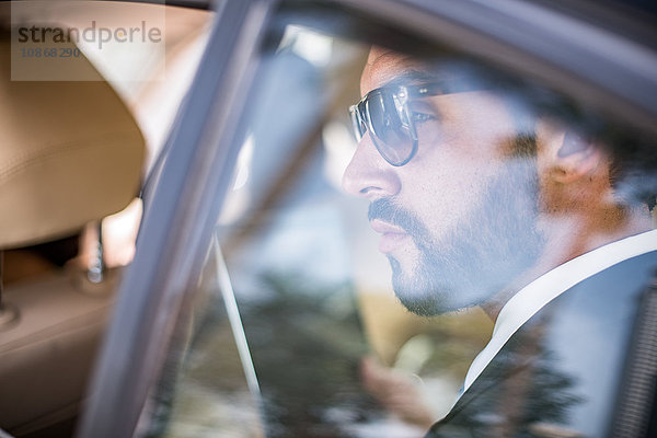 Junger Geschäftsmann mit Sonnenbrille  der vom Rücksitz aus dem Autofenster schaut  Dubai  Vereinigte Arabische Emirate