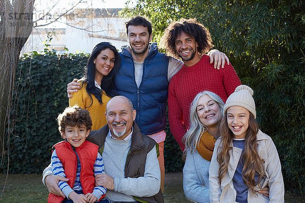 Mehrgenerationen-Familie kauert sich zusammen und schaut lächelnd in die Kamera