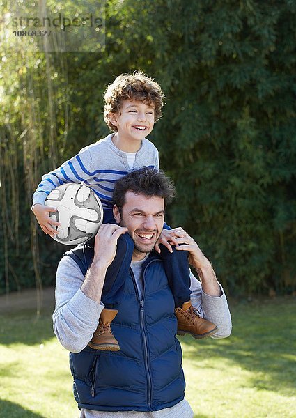 Vater trägt lächelnden Sohn mit Fussball auf den Schultern