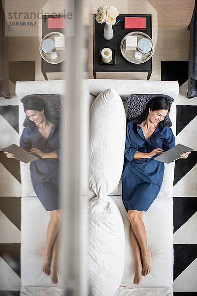 Draufsicht einer auf einem Hotelzimmersofa liegenden Frau mit digitalem Tablet  Dubai  Vereinigte Arabische Emirate