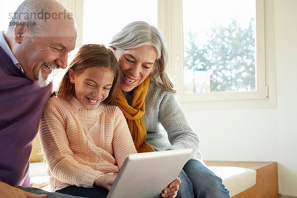 Großeltern am Fenstersitz mit digitalem Tablett  die Enkelin schaut lächelnd nach unten