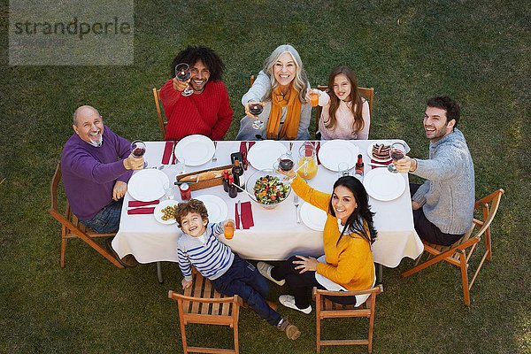 Draufsicht auf eine Mehrgenerationen-Familie  die im Freien speist  in die Kamera schaut und lächelnd anstößt