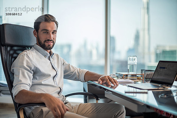 Porträt eines Geschäftsmannes am Schreibtisch mit Fensteransicht des Burj Khalifa  Dubai  Vereinigte Arabische Emirate