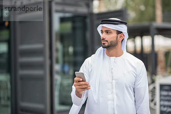 Mann trägt traditionelle Kleidung aus dem Nahen Osten mit Smartphone  Dubai  Vereinigte Arabische Emirate