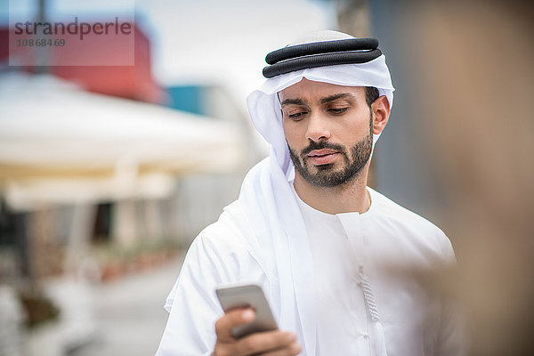 Mann in traditioneller Kleidung aus dem Nahen Osten liest Smartphone-Text  Dubai  Vereinigte Arabische Emirate