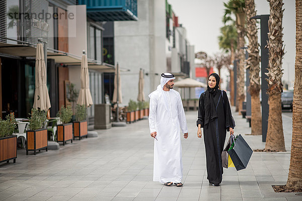 Einkaufspaar aus dem Nahen Osten trägt traditionelle Kleidung mit Einkaufstaschen  Dubai  Vereinigte Arabische Emirate