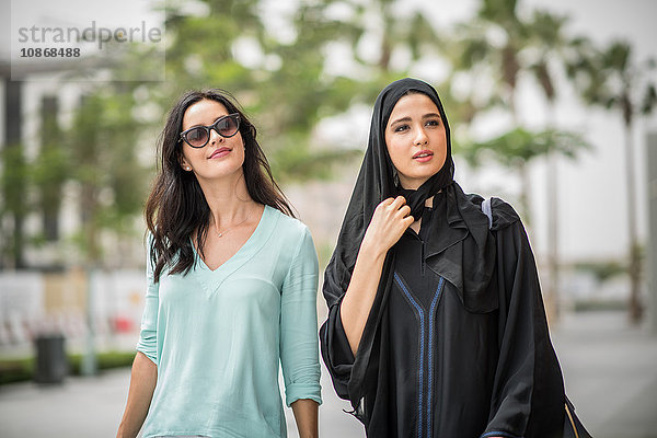Junge Frau aus dem Nahen Osten in traditioneller Kleidung geht mit einer Freundin die Straße entlang  Dubai  Vereinigte Arabische Emirate