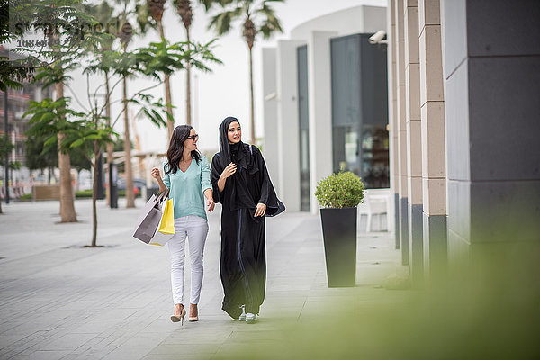 Junge Frau aus dem Nahen Osten in traditioneller Kleidung geht mit einer Freundin die Straße entlang  Dubai  Vereinigte Arabische Emirate