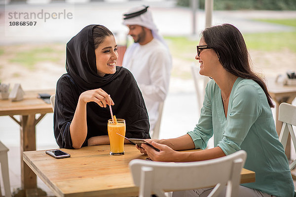 Junge Frau aus dem Nahen Osten in traditioneller Kleidung im Gespräch mit einer Freundin im Café  Dubai  Vereinigte Arabische Emirate