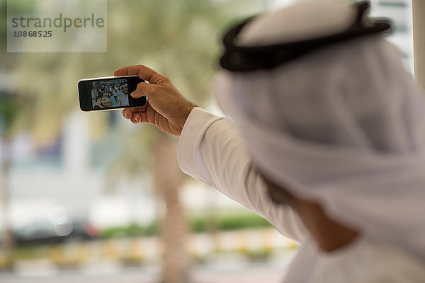 Über die Schulter eines Mannes aus dem Nahen Osten  der mit Freunden in einem Cafe ein Smartphone mitnimmt  Dubai  Vereinigte Arabische Emirate