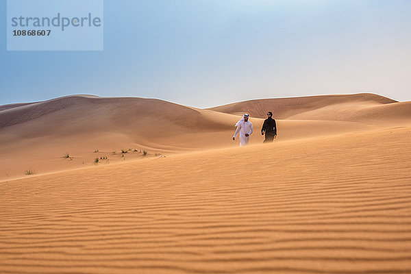 Fernansicht eines Paares in traditioneller nahöstlicher Kleidung  das auf einer Wüstendüne spazieren geht  Dubai  Vereinigte Arabische Emirate