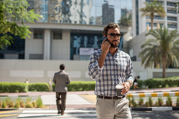 Junger Mann auf Fußgängerüberweg im Gespräch auf Smartphone  Dubai  Vereinigte Arabische Emirate