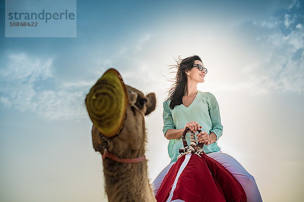 Niedrigwinkelaufnahme eines weiblichen Touristen auf einem Kamel in der Wüste  Dubai  Vereinigte Arabische Emirate