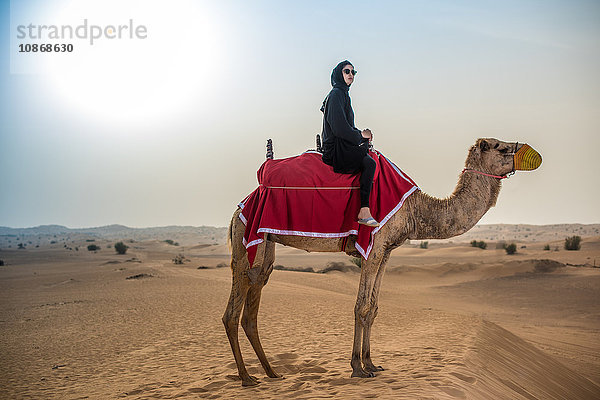 Junge Frau in traditioneller nahöstlicher Kleidung auf Kamel in der Wüste  Dubai  Vereinigte Arabische Emirate