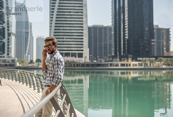 Junger Mann lehnt an Ufergeländer gelehnt und spricht über Smartphone  Dubai  Vereinigte Arabische Emirate