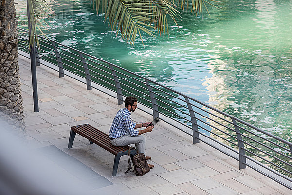 Hochwinkelansicht eines jungen Mannes  der am Wasser sitzt  mit einem digitalen Tablet  Dubai  Vereinigte Arabische Emirate