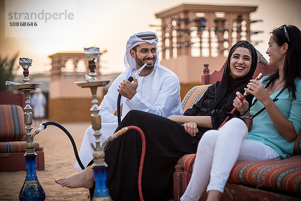 Einheimisches Paar in traditioneller Kleidung raucht Shisha auf dem Sofa mit einer Touristin  Dubai  Vereinigte Arabische Emirate