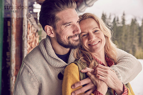 Porträt eines romantischen Paares  das im Winter vor einem Blockhaus steht  Elmau  Bayern  Deutschland