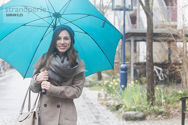 Porträt einer jungen Frau im Freien  die einen blauen Regenschirm hält