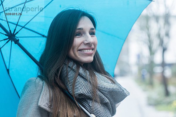 Porträt einer jungen Frau im Freien  die einen blauen Regenschirm hält