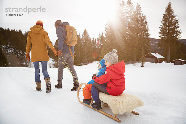Rückansicht von Eltern  die ihre Söhne auf dem Schlitten in der Schneelandschaft ziehen  Elmau  Bayern  Deutschland