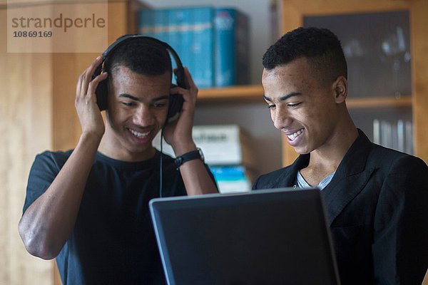 Zwillingsbrüder zu Hause  schauen auf den Laptop  tragen Kopfhörer  lächeln