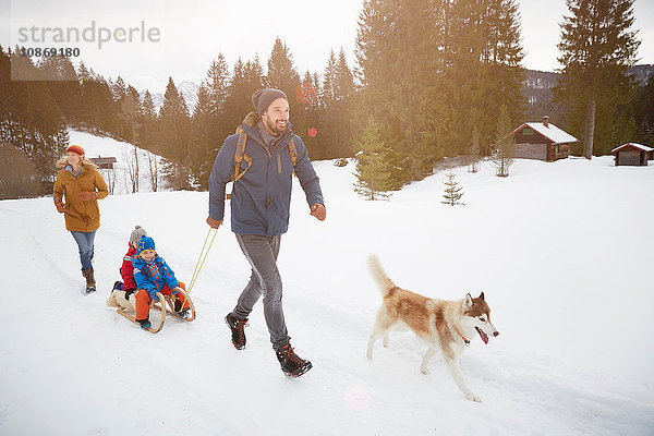 Eltern mit Schlittenhunden  die ihre Söhne auf dem Schlitten in der verschneiten Landschaft ziehen  Elmau  Bayern  Deutschland