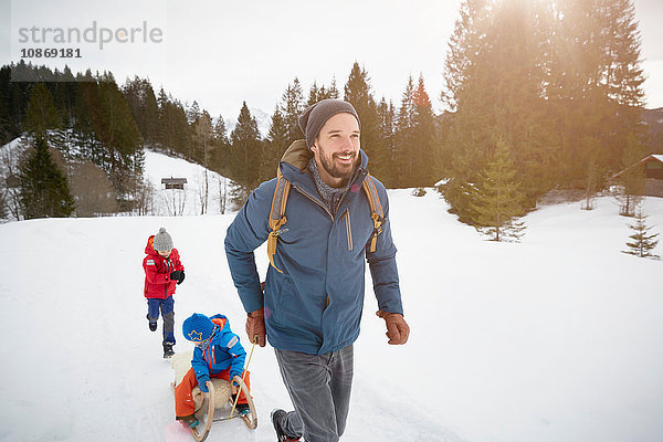 Junger Mann zieht Söhne auf Schlitten in schneebedeckter Landschaft  Elmau  Bayern  Deutschland