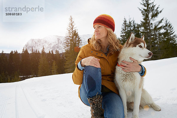 Frau sitzt mit Husky in schneebedeckter Landschaft  Elmau  Bayern  Deutschland