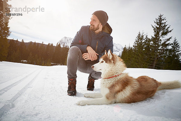 Junger Mann kauert mit Husky in schneebedeckter Landschaft  Elmau  Bayern  Deutschland